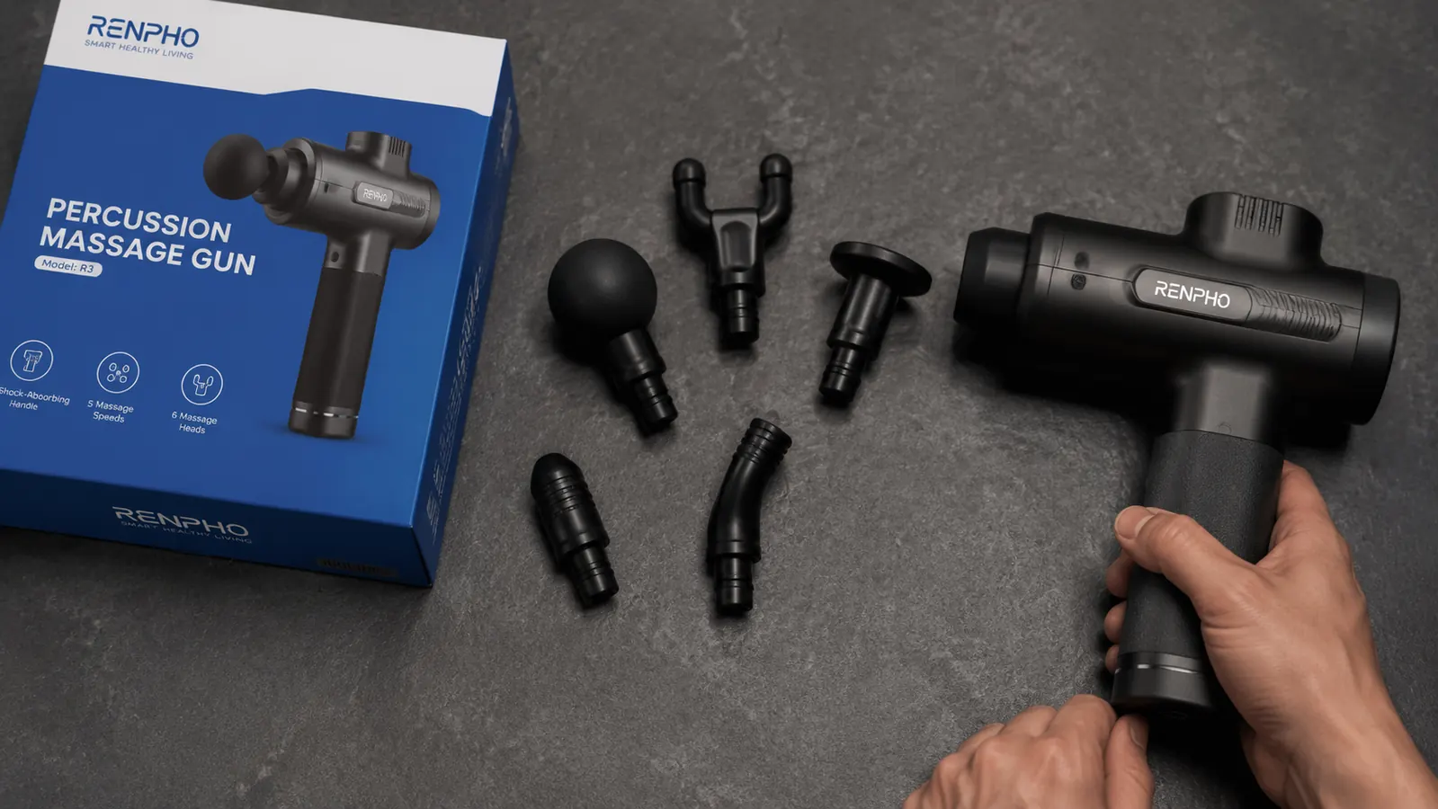 Flat lay of the RENPHO massage gun with all six attachment heads arranged beside it on a dark surface