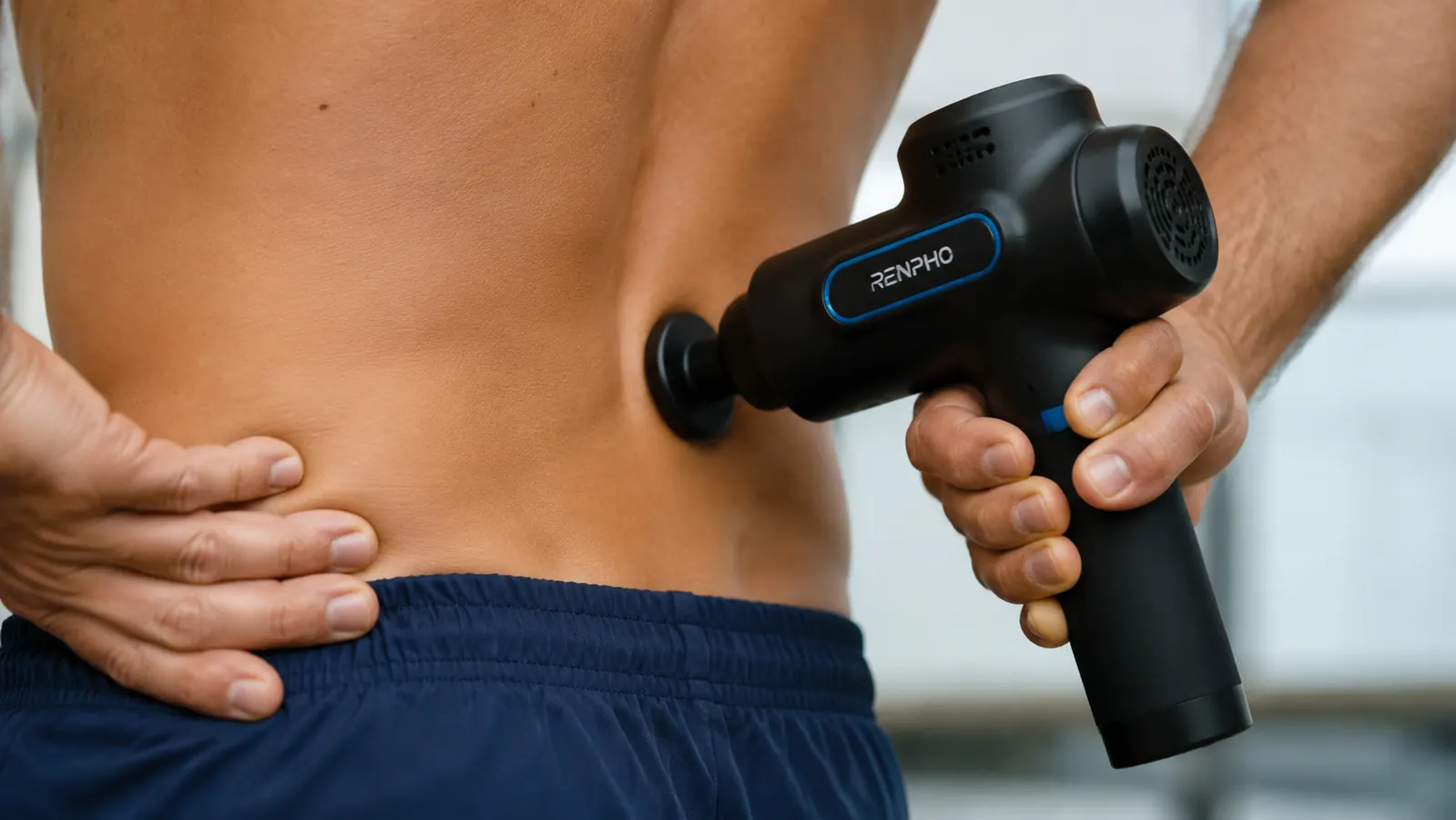 Close-up of a RENPHO massage gun with the flat head attachment pressed against the erector muscles beside the lower spine